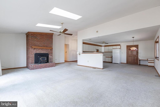 unfurnished living room featuring a ceiling fan, light carpet, a skylight, and baseboards