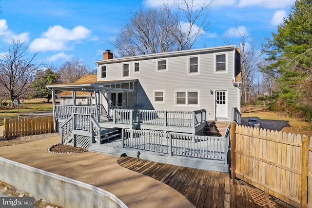 back of property with a chimney, a wooden deck, and fence