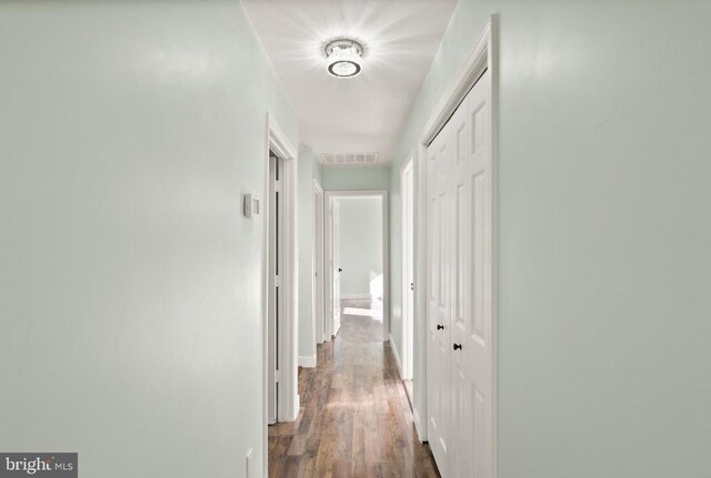 hallway featuring visible vents, baseboards, and wood finished floors