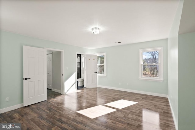 unfurnished bedroom with ensuite bath, dark wood-style floors, and baseboards