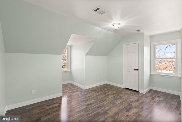 additional living space with vaulted ceiling, baseboards, visible vents, and dark wood-style flooring