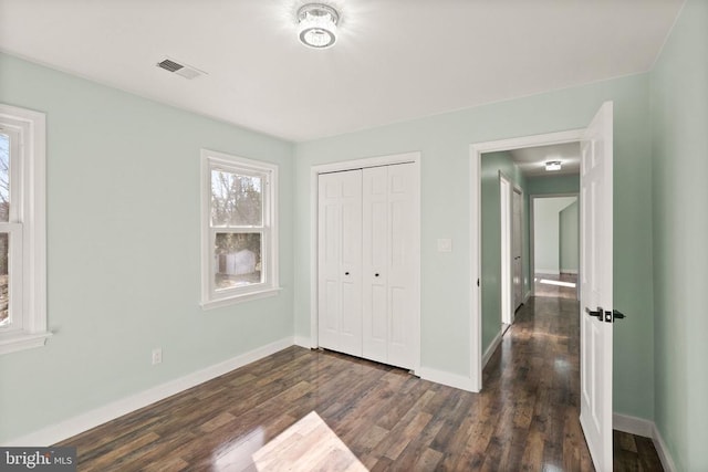 unfurnished bedroom featuring visible vents, baseboards, a closet, and dark wood-style flooring