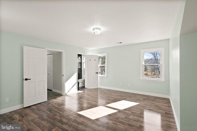 unfurnished bedroom featuring baseboards, ensuite bathroom, and dark wood-style flooring