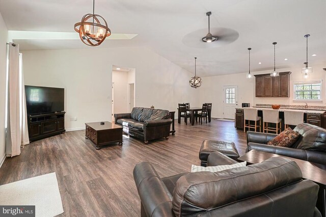 living room featuring dark wood-style floors, lofted ceiling, a chandelier, a ceiling fan, and baseboards