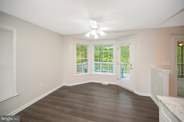 unfurnished room with dark wood-style flooring, a ceiling fan, and baseboards