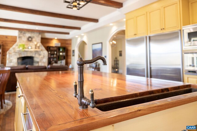 kitchen with wooden counters, beam ceiling, open floor plan, arched walkways, and built in refrigerator