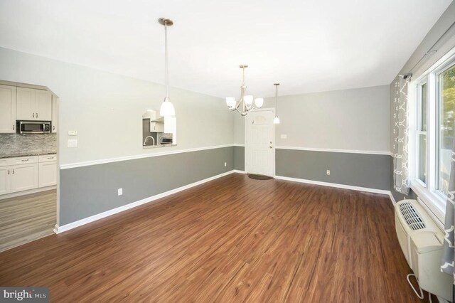 unfurnished living room featuring dark hardwood / wood-style floors, a wall mounted AC, and a chandelier