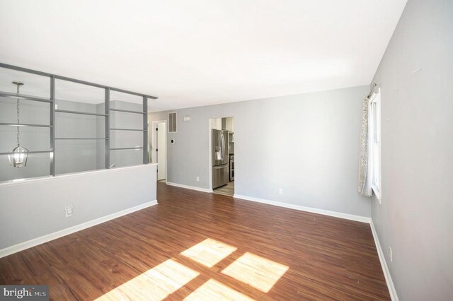 spare room featuring an inviting chandelier and dark hardwood / wood-style floors