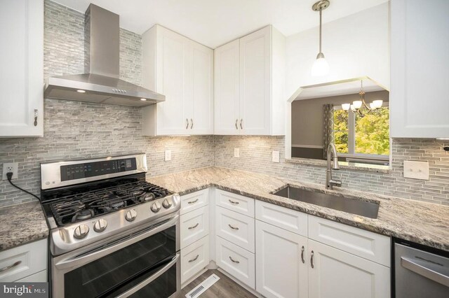 kitchen featuring wall chimney range hood, sink, stainless steel appliances, light stone counters, and white cabinets