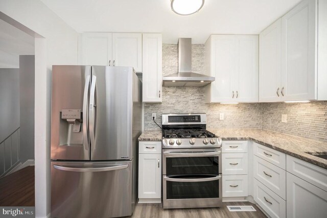 kitchen with stainless steel appliances, wall chimney range hood, and white cabinets