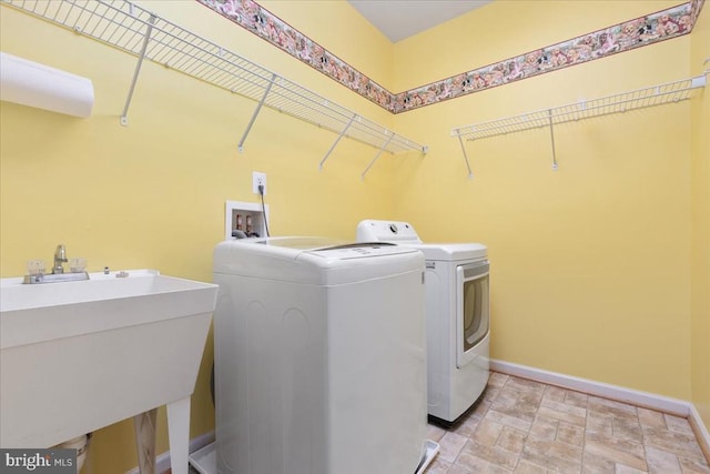  - washroom featuring a sink, laundry area, stone finish floor, washer and clothes dryer, and baseboards