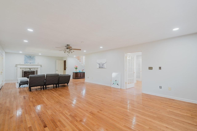 living area with light wood-type flooring, ceiling fan, recessed lighting, a premium fireplace, and baseboards