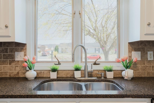 kitchen view of a sink, white cabinetry, and dark stone countertops