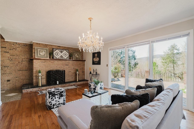living room featuring wood-type flooring, a chandelier, ornamental molding, a textured ceiling, and a fireplace