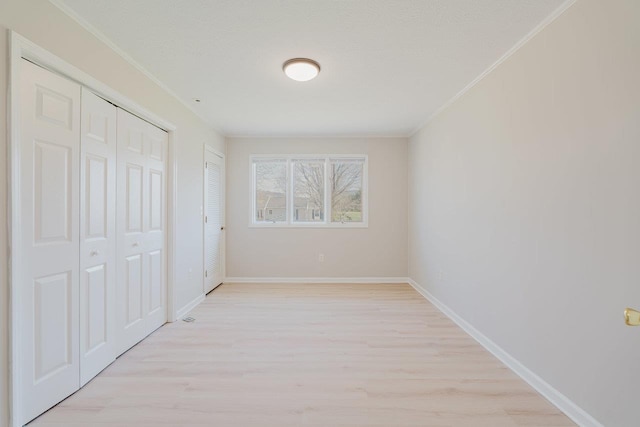 unfurnished bedroom featuring light wood finished floors, ornamental molding, baseboards, and multiple closets
