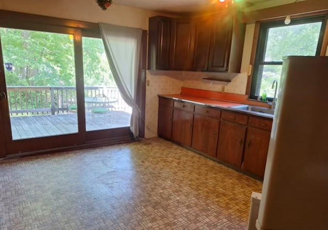 kitchen with freestanding refrigerator, light countertops, a sink, and brown cabinetry