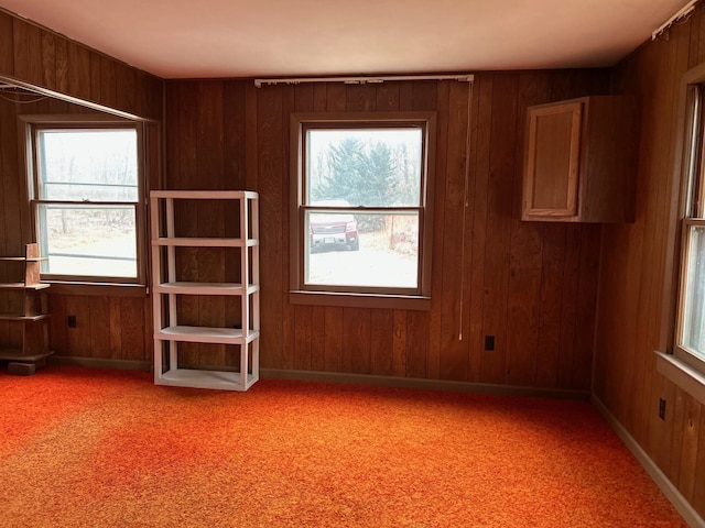 spare room with healthy amount of natural light, wood walls, and light carpet