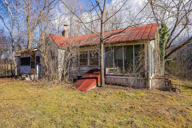 rear view of property featuring a chimney, a sunroom, and metal roof