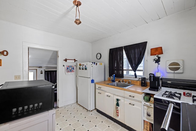 kitchen featuring light floors, freestanding refrigerator, a sink, white cabinets, and gas range