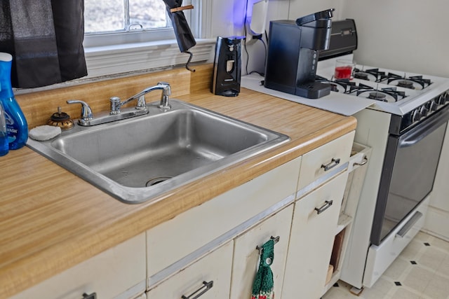 kitchen with a sink, white cabinetry, white gas stove, and light countertops