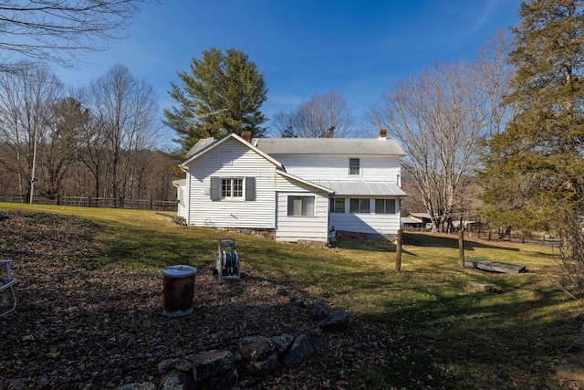 rear view of property featuring a yard, fence, a chimney, and metal roof