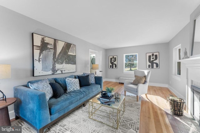 living room featuring a fireplace with flush hearth, baseboards, and wood finished floors