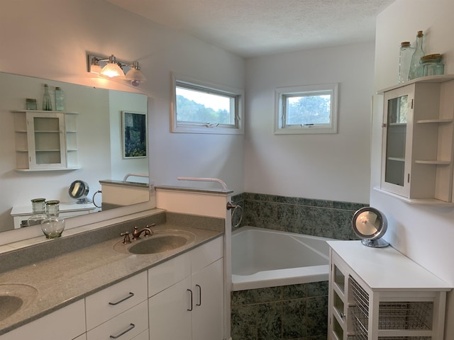 bathroom featuring vanity, a textured ceiling, and tiled tub