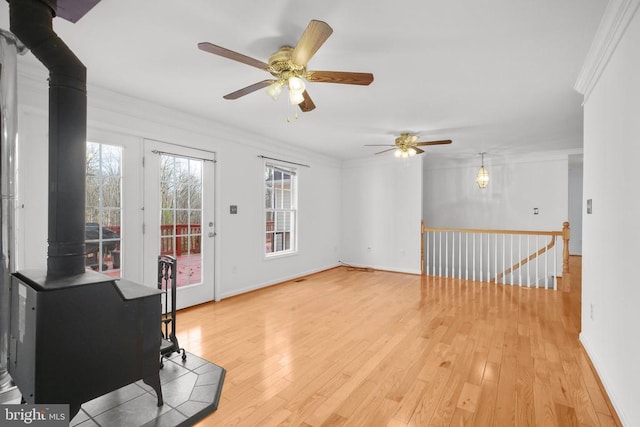 interior space featuring ornamental molding, a wood stove, a ceiling fan, and light wood-style floors