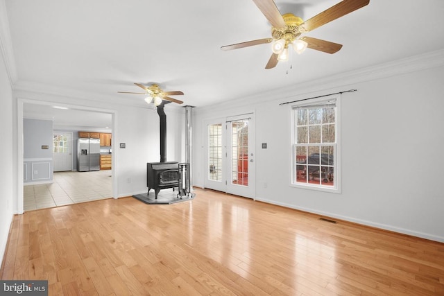 unfurnished living room featuring a healthy amount of sunlight, light wood-style flooring, ornamental molding, ceiling fan, and a wood stove