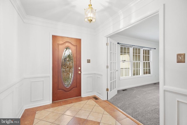 tiled foyer featuring a wainscoted wall, a notable chandelier, crown molding, and a decorative wall