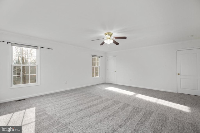 empty room with a wealth of natural light, visible vents, ceiling fan, and ornamental molding