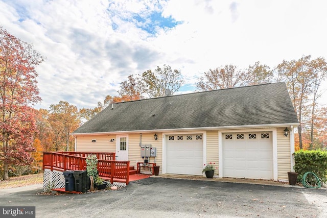 exterior space featuring a detached garage, a shingled roof, and a wooden deck