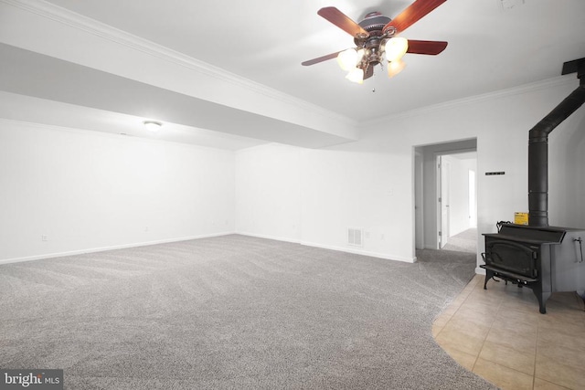 unfurnished living room with carpet, ornamental molding, ceiling fan, baseboards, and a wood stove
