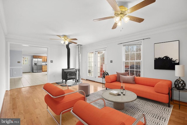 living room with a wood stove, a ceiling fan, light wood-style floors, and crown molding