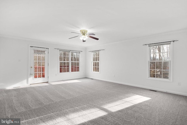 carpeted spare room with ornamental molding, a ceiling fan, visible vents, and baseboards