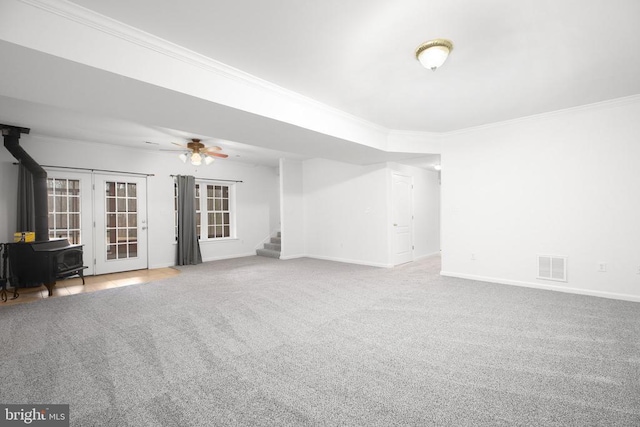 empty room featuring crown molding, a wood stove, visible vents, baseboards, and stairs