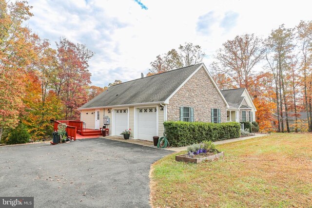 view of side of property featuring driveway, a yard, an attached garage, and stone siding