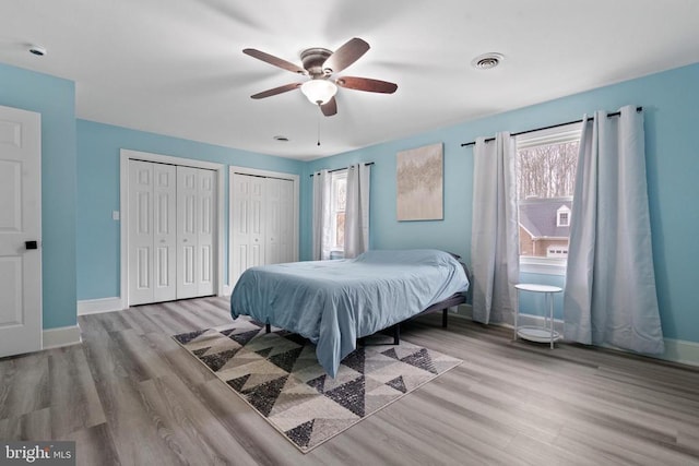 bedroom featuring visible vents, ceiling fan, baseboards, multiple closets, and wood finished floors