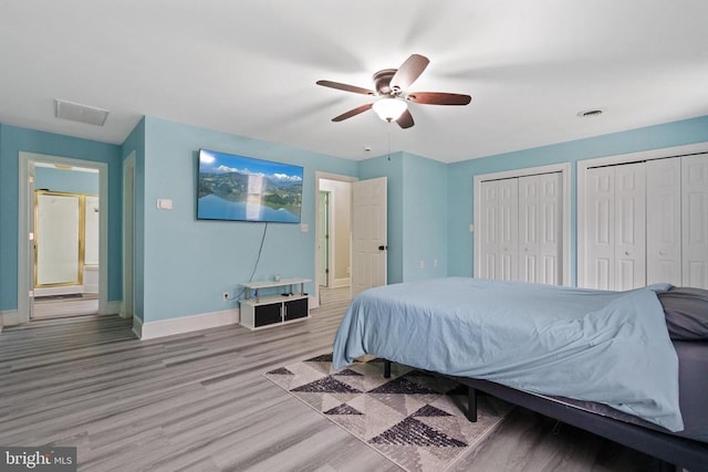 bedroom featuring visible vents, baseboards, light wood-type flooring, and two closets