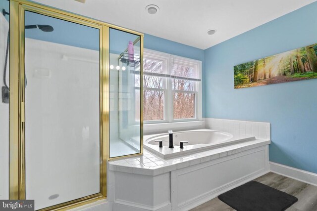 bathroom with a bath, a stall shower, baseboards, and wood finished floors