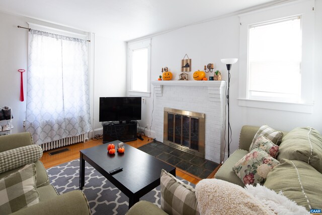 living room with wood-type flooring, a brick fireplace, and a healthy amount of sunlight