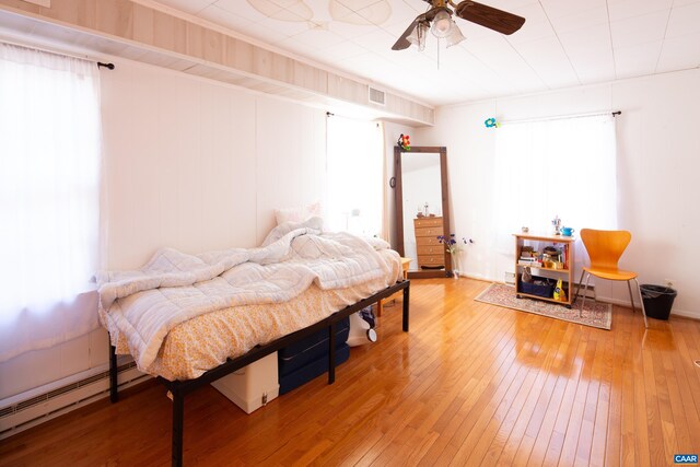 bedroom with multiple windows, hardwood / wood-style flooring, a baseboard radiator, and ceiling fan