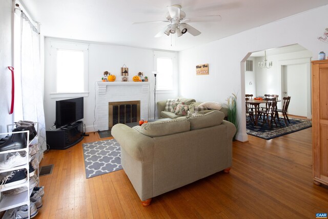 living room with a brick fireplace, wood-type flooring, and ceiling fan