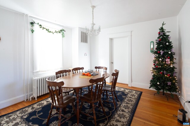 dining area featuring wood-type flooring, radiator, and a notable chandelier