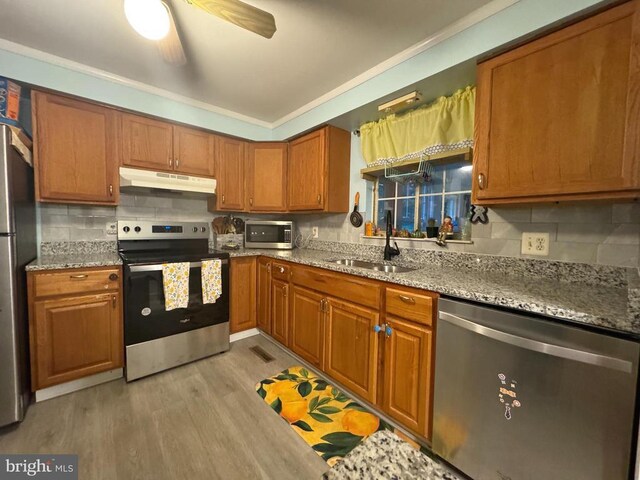 kitchen featuring sink, decorative backsplash, stainless steel appliances, light stone countertops, and light hardwood / wood-style flooring