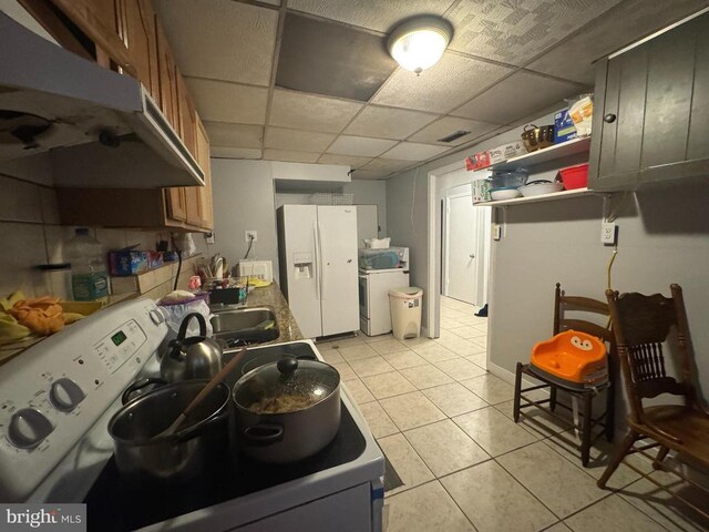 kitchen with light tile patterned floors, white appliances, a paneled ceiling, and washer / dryer