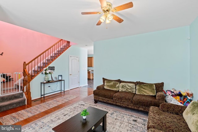 living room with a ceiling fan, baseboards, stairway, and wood finished floors