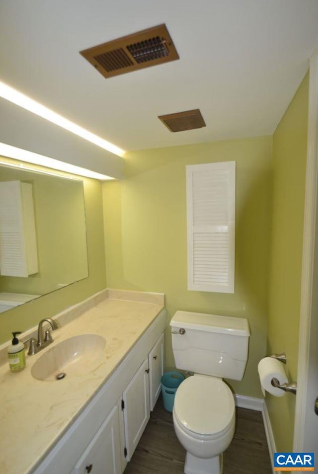 bathroom with visible vents, toilet, vanity, wood finished floors, and baseboards