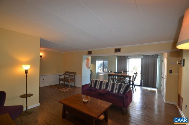 living room with ornamental molding, visible vents, baseboards, and wood finished floors