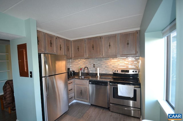 kitchen featuring a sink, appliances with stainless steel finishes, backsplash, dark wood-style floors, and dark countertops